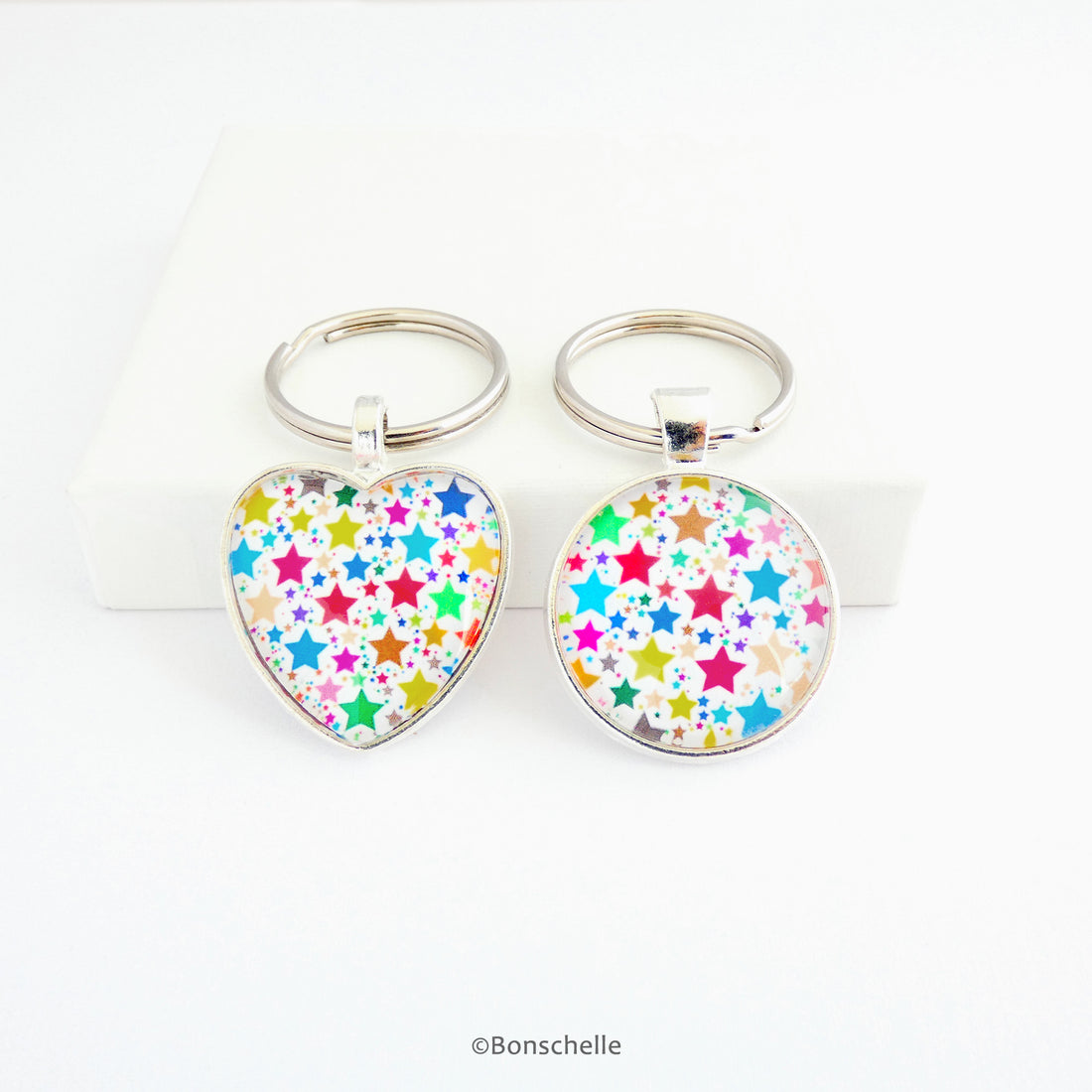 Silver toned metal heart and round shaped keyrings with a multicoloured bright star pattern