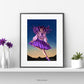 An original art print featuring a young girl in Lolita fashion dancing happily in the snow against an evening sky. The poster is mounted on white with a black frame. It sits on a white shelf. To one side are flowers in vases and the other a cactus in a flowerpot.