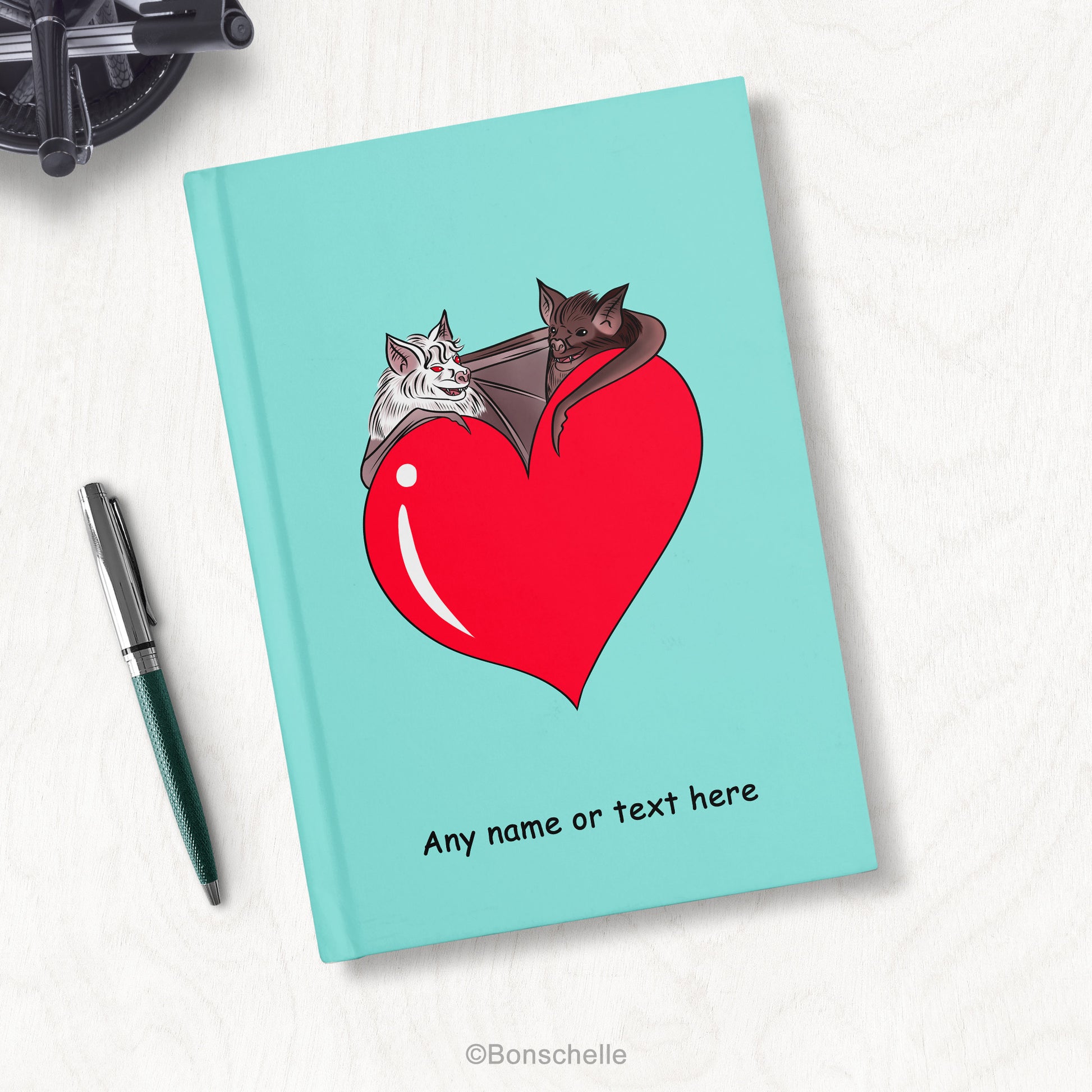 Cute Bat Couple with Love Heart Personalised Hardback Notebook, on a wood desk with pens