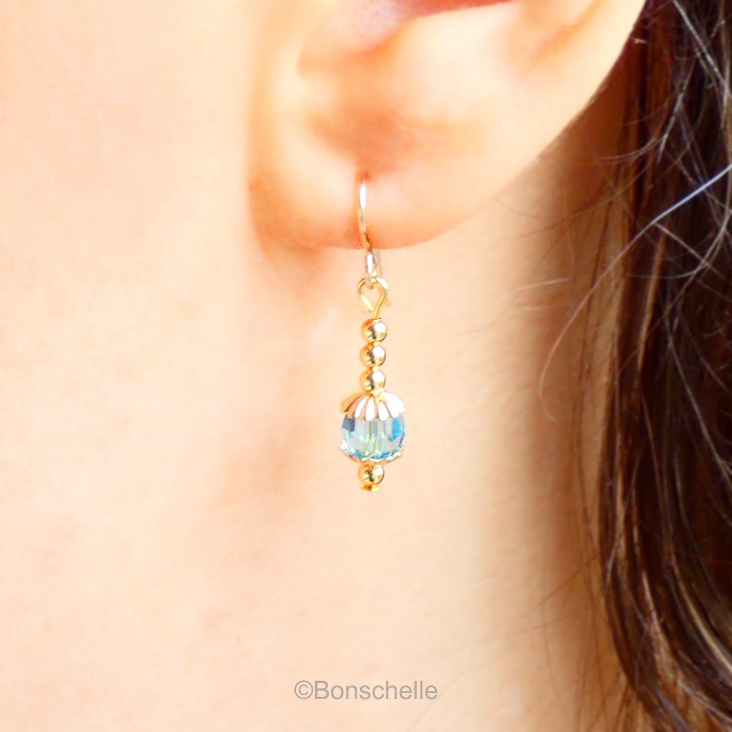 Handmade dangle earrings made with turquoise coloured Swarovski cut glass crystal faceted beads, small gold toned beads and 14K gold filled earwires shown being worn.