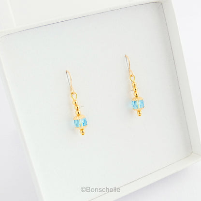 Handmade dangle earrings made with turquoise coloured Swarovski cut glass crystal faceted beads, small gold toned beads and 14K gold filled earwires shown in a jewellery box