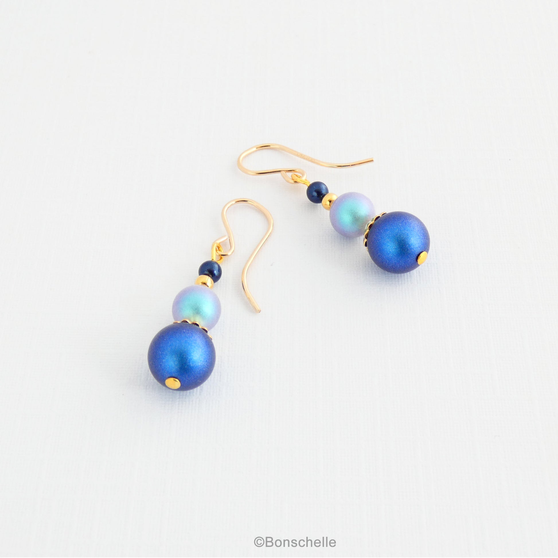 Dark, medium, and pale blue Swarovski crystal pearl beads with 14K gold filled earwires for women lying on a surface