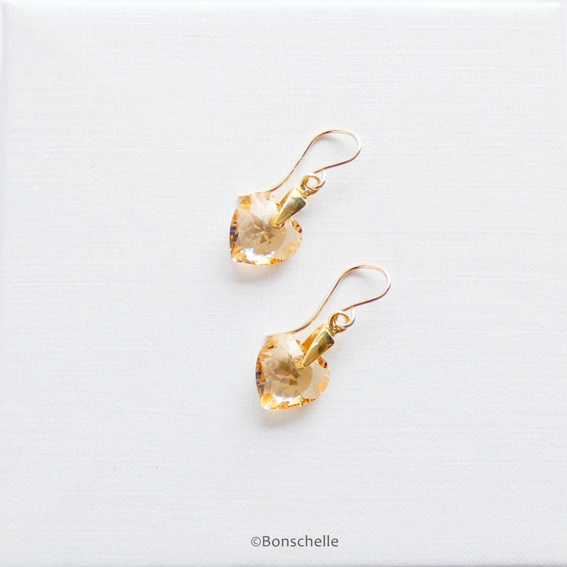 Handmade earrings with pale golden bronze toned Swarovski crystal heart earrings and 14K gold filled earwires laying on a surface