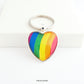 Heart shaped silver metal keyrings with a colourful bright rainbow stripe pattern capped with a clear glass cabochon.