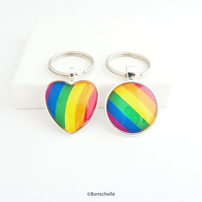 Heart shaped and round shaped silver metal keyrings with a colourful bright rainbow stripe pattern capped with a clear glass cabochon.