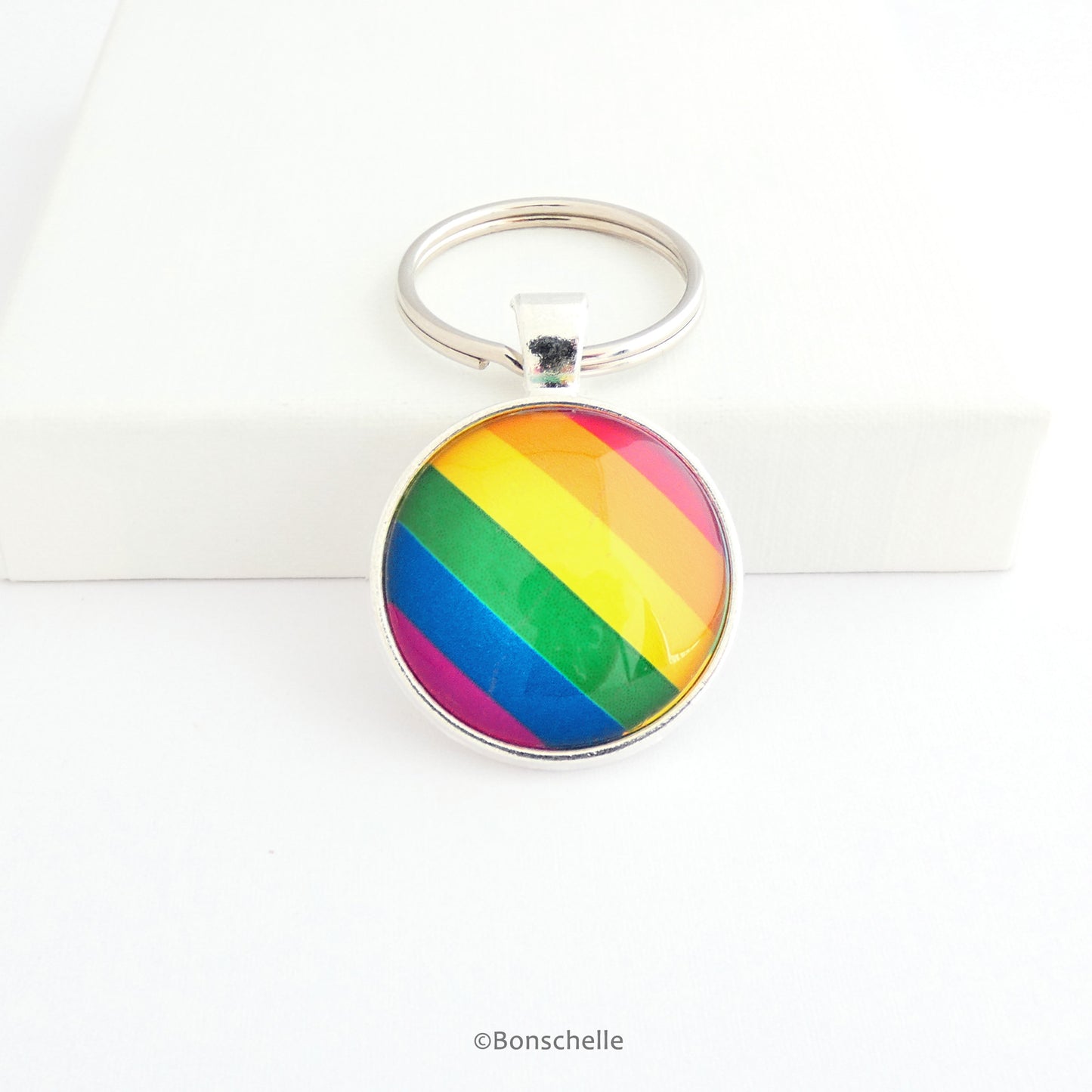 Round shaped silver metal keyrings with a colourful bright rainbow stripe pattern capped with a clear glass cabochon.