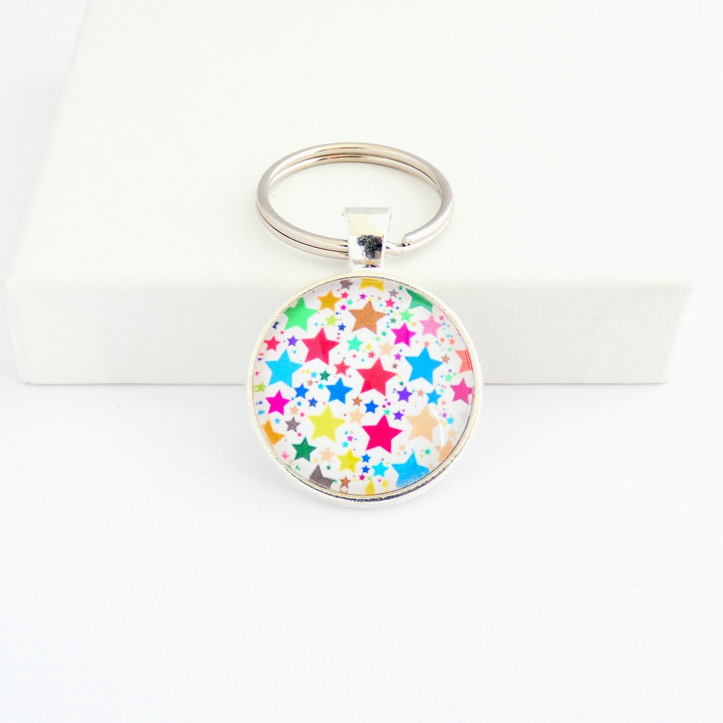 A round shaped silver toned metal keyring with a colourful star pattern design capped wtih a clear glass cabochon
