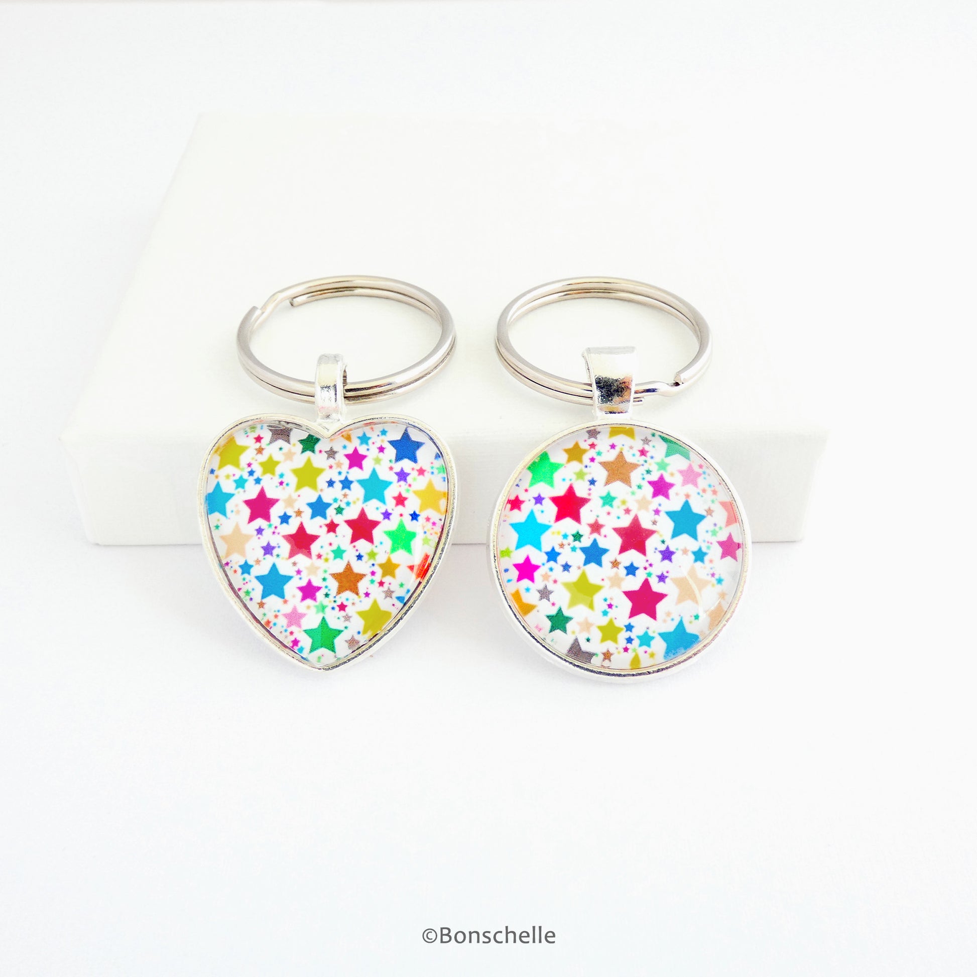 Heart shaped and a round shaped silver toned metal keyring with a colourful star pattern design capped wtih a clear glass cabochon.