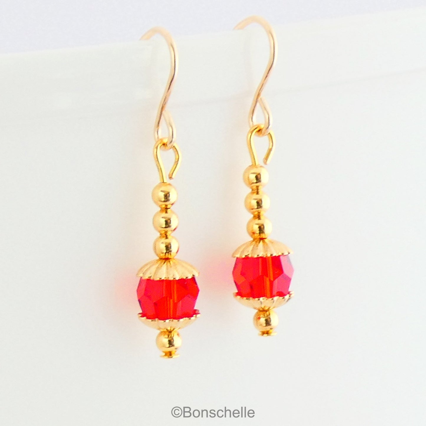 Drop earrings with a single bright red Swarovksi crystal beads, 3 smaller gold toned metal beads and 14K gold filled earwires.