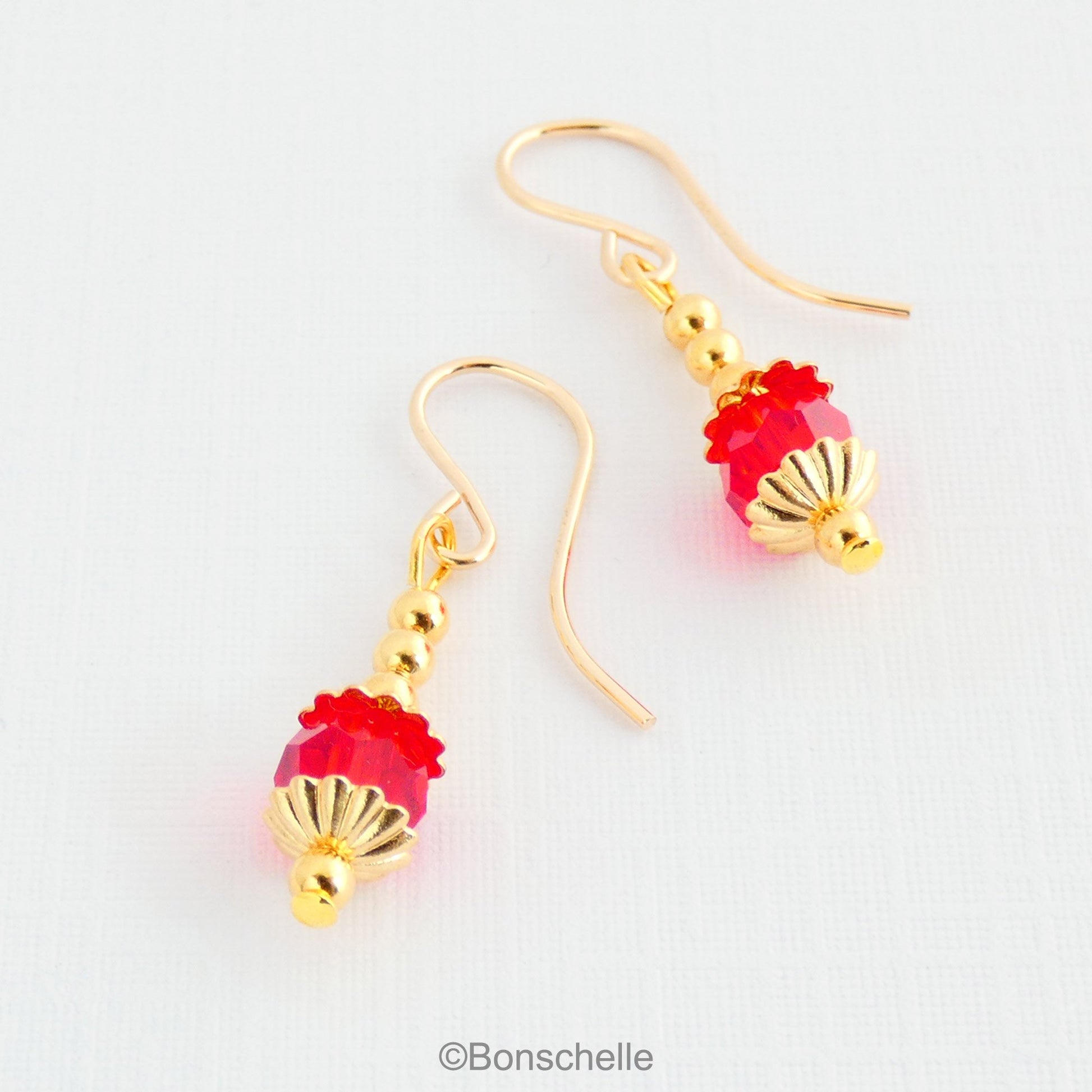 Drop earrings with a single bright red Swarovksi crystal beads, 3 smaller gold toned metal beads and 14K gold filled earwires.