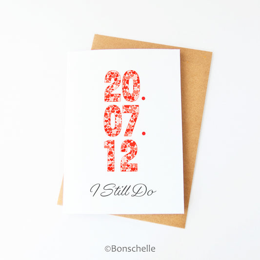 Front view of a handmade greeting Card with a personalised date in heart patterned numbers and the words 'I Still Do' beneath on the front, with a brown envelope.