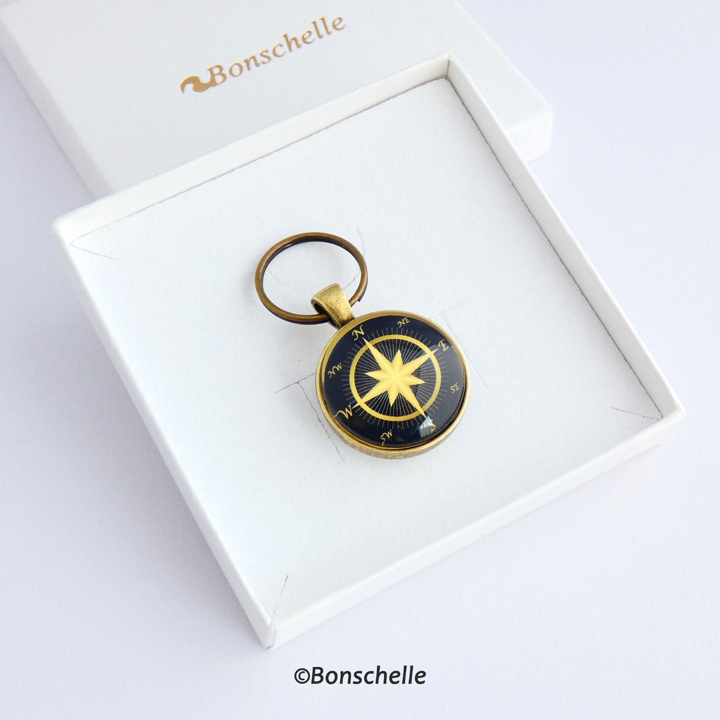 Front view of a personalised bronze metal round double sided keyring, with light bronze coloured compass rose on the front against a navy blue background  laying in a white gift box