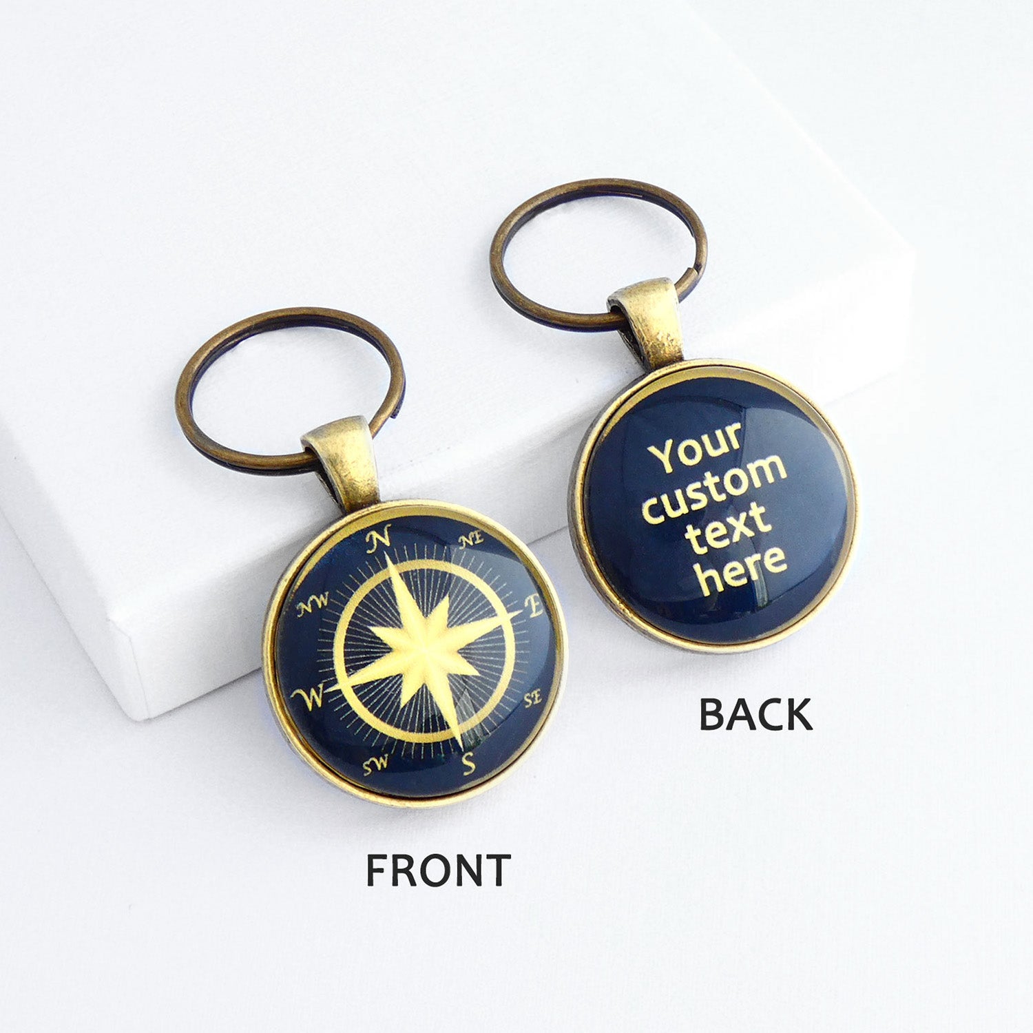 Front and back views of a personalised bronze metal round double sided keyring, with light bronze coloured compass rose on the front against a navy blue background, and the back wtih light bronze coloured text against a navy blue background.