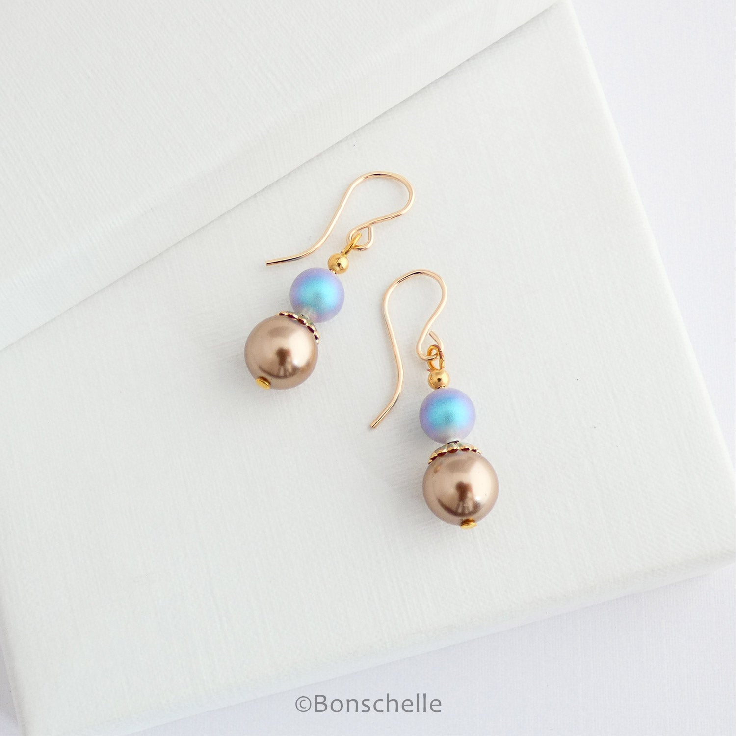 Women's handmade bronze and sky blue pearl earrings laying on a jewellery box